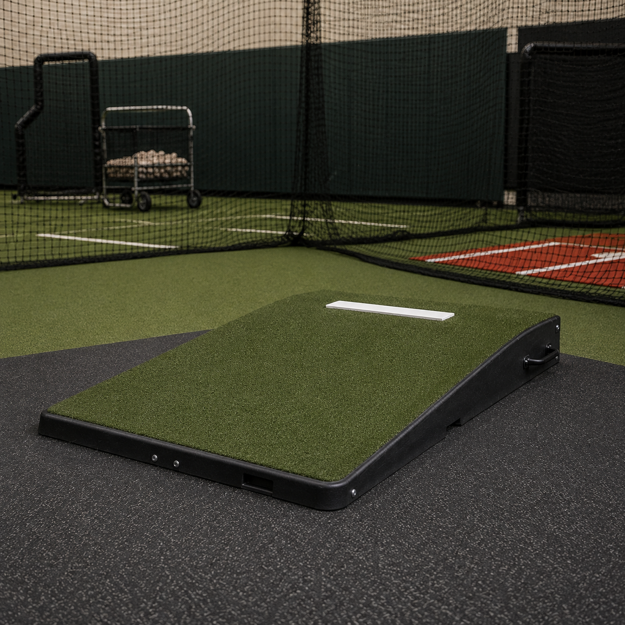 Portable 10-inch regulation pitching mound with turf surface and fiberglass core deployed in an indoor batting cage for high school baseball pitching practice